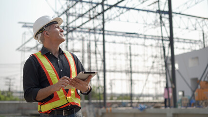 senior construction worker or architect using digital tablet checking structure in construction site outdoors Hand shading with Hot weather and sunny. builders in hard hat inspecting and working 
