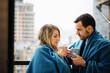 © olezzo - Young beautiful couple family man and woman sitting on the windowsill drinking coffee wrapped in blue blankets, romantic romantic at the hotel