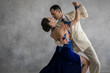 Couple of professional tango dancers in elegant suit and blue dress pose in a dancing movement on grey background. Handsome man and woman dance looking eye to eye.