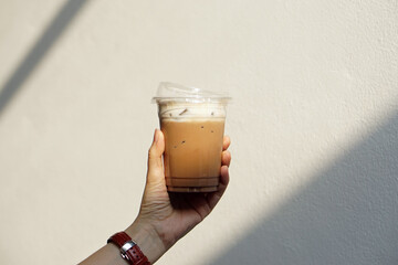 Iced mocha - Holding glass of coffee latte mixed with cocoa on wooden table and blurred background.