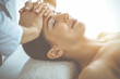 © rogerphoto - Beautiful brunette woman enjoying facial massage with closed eyes in sunny spa center. Relaxing treatment and cosmetic medicine concepts
