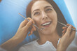 © rogerphoto - Smiling brunette woman being examined by dentist at dental clinic. Hands of a doctor holding dental instruments near patient's mouth. Healthy teeth and medicine concept