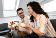 © Zoran Zeremski - Smiling couple sitting on sofa and eating fast food salad at home.