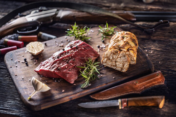 Wall Mural - Nutrient rich raw deer venison prepared for a cooking process on a rustic wooden desk with roasted garlic, rosemary and huntig accesories like shot gun and ammunition