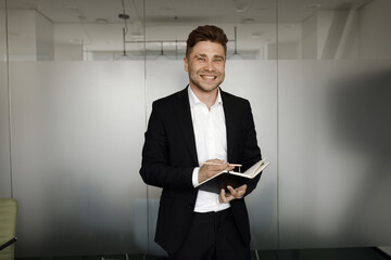 Wall Mural - A young, handsome man in a black suit, smiling. Close-up portrait of a businessman.