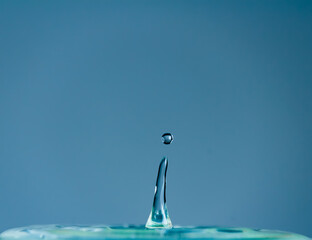 Sticker - Water droplet falling and splashing on blue background. Macro nature photo