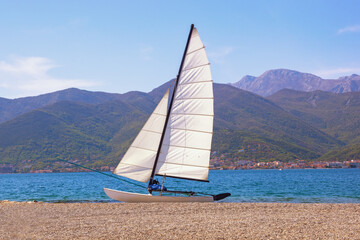 Sailboat with white sail on beach. Vacations and recreation concept. Montenegro, Adriatic Sea, Bay of Kotor