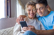 © Daniel - Smiling middle-aged 40s mother rest with grown-up son using smartphone together, happy young man enjoy family weekend with mom browsing wireless Internet on cellphone, have fun at home