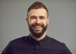 © Studio Romantic - Headshot of cheerful businessman in black dress shirt with positive beaming smile on friendly open face. Studio portrait of happy stylish bearded young man with modern short haircut with shaved sides
