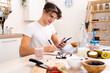 © Giorgio Fochesato/Westend61 - Young man with smart phone writing on notepad while sitting at table in kitchen