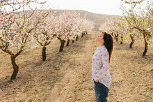 Young woman standing with hand in pocket at almond trees