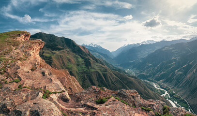 Colorful summer landscape with silhouettes of big rocky mountains and epic deep gorge with river.The edge of a rocky cliff with a beautiful panoramic view of the gorge.