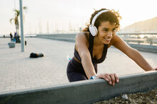 Smiling Sportswoman Listening Music Through Headphones While Exercising On Bridge