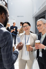 african american man showing business card near smiling interracial colleagues