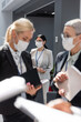 © LIGHTFIELD STUDIOS - selective focus of asian businesswoman in medical mask near colleagues talking on blurred foreground