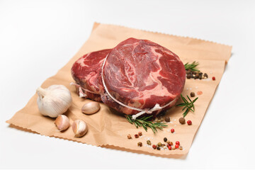 Fresh raw pieces of beef meat with ingredients for cooking on a wrapping paper on white background