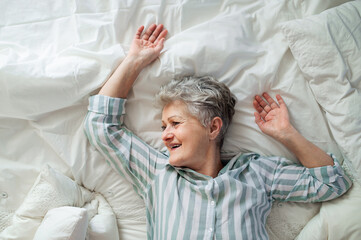 Wall Mural - Top view of happy senior woman in bed at home, relaxing.