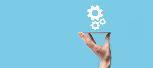 Male hand holding cog gears icon ,mechanism icon on virtual screens on blue background. Automation Software Technology Process System Business concept. Banner