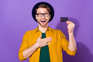 Portrait of attractive amazed cheerful guy holding plastic card paypass fast isolated over bright violet purple color background