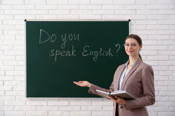 Canvas Print - Teacher near green chalkboard with inscription Do You Speak English? in classroom