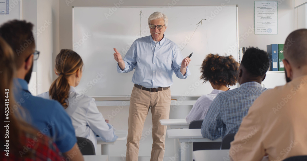 Senior male teacher with a group of students teaching in classroom. - obrazy, fototapety, plakaty 