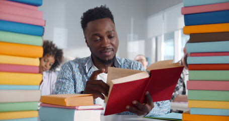 Portrait of smiling afro-american young man with pile of books studying in classroom