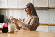 © Drobot Dean - Mature smiling woman using cellphone while having breakfast