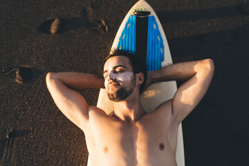 Muscular eyes closed man sunbathing on sandy beach during sunset