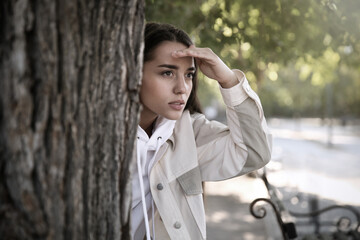 Wall Mural - Young woman spying on her boyfriend in park. Cheating concept