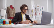 © TommyStockProject - Male fashion designer look at laptop working with sketches in studio atelier.