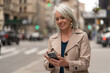 © blvdone - Mature caucasian woman in city walking street using cellhpone