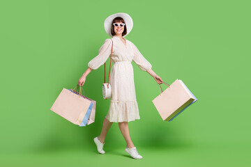 Sticker - Full length body size photo woman in sunglass walking on shopping center with bags smiling isolated pastel green color background