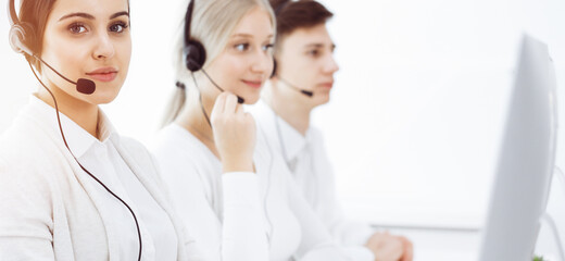 Wall Mural - Call center in sunny office. Group of diverse operators at work. Beautiful woman in headset communicating with customers of telemarketing service