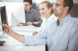 © Iryna - Business people working together in modern office. Happy smiling adult businessman using pc computer with colleagues. Teamwork and partnership concept