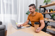 © LIGHTFIELD STUDIOS - positive, disabled man holding coffee to go while typing on laptop near cellphone with blank screen