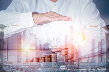 double exposure image concept, hand holding ligh blub coins idea business industrial technology future plant and enegry graphic design. Oil, gas and petrochemical refinery factory with background.