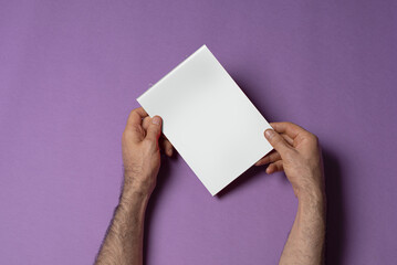 Poster - Hands holding a small a5 catalog with blank cover on purple background