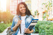 © wpadington - Portrait of beautiful happy smiling african american girl student posing outdoors with a backpack and pile of books and tablet computer in hands