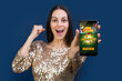 © wpadington - Happy woman in sparkling dress showing smartphone screen with online casino website interface to the camera and clenching fist in winner gesture