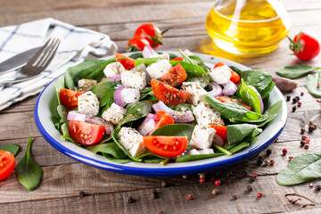 Wall Mural - Healthy food. Greek salad with spinach, tomato, sweet pepper, red onion, feta cheese on a wooden table.