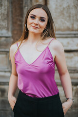 Wall Mural - Vertical shot of a young blonde female model posing on the sidewalk in a pink blouse and black pants