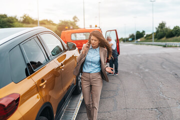 Wall Mural - Elegant middle age business woman calling someone while towing service helping her on the road. Roadside assistance concept..