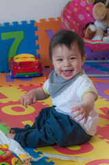 Wall Mural - Vertical shot of a cute smiling Swiss baby boy playing with toys on a rubber mat