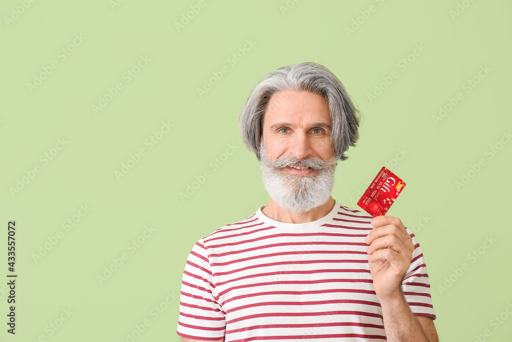 Senior man with gift card on color background