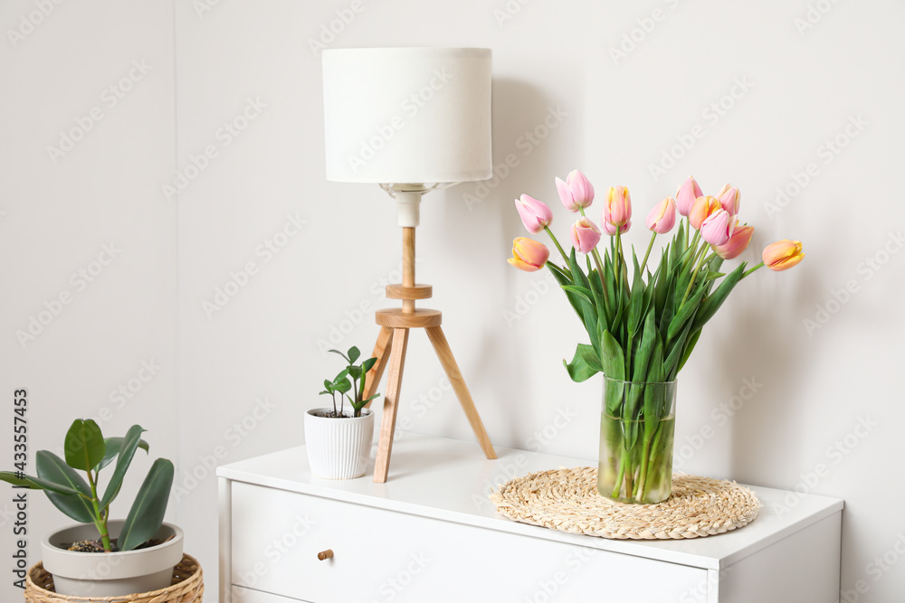 Bouquet of tulip flowers on chest of drawers near white wall - obrazy, fototapety, plakaty 