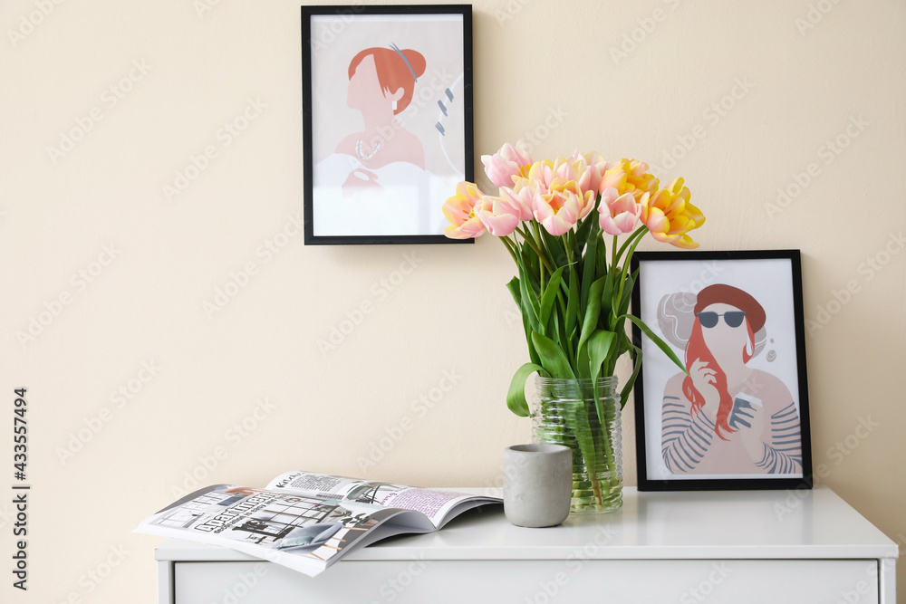 Bouquet of tulip flowers and magazine on chest of drawers near color wall
