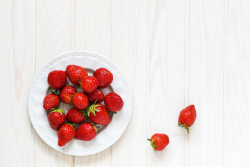 plate with fresh strawberry berries on a wooden light background and two separately lying berries