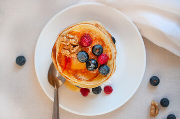 Wall Mural - Flat lay of freshly cooked delicious pancakes with honey, walnut, raspberries and blueberries for breakfast.