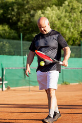 Wall Mural - An adult man plays tennis on a street court on a sunny day. Sports and active lifestyle. Vertical.