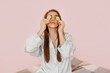 © Daria Lukoiko - Girl make homemade face beauty masks. Cucumbers for the freshness of the skin around the eyes. Woman take care of youthful skin. Model laughing and having fun in spa on pink background